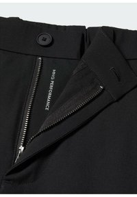 Pantaloni neri con zip e chiusura a bottone. L'interno presenta dettagli con logo e un tessuto liscio e strutturato.