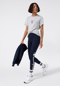 Szara koszulka z krótkim rękawem z grafiką "love", granatowe legginsy z białym logo, białe sneakersy z czarnymi akcentami i w paski skarpetki.
