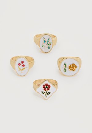 Quatre bagues en or avec faces en émail blanc présentant des motifs colorés floraux et d'oiseaux, disposées sur un fond blanc.