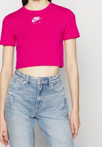Fuchsiové zkrácené tričko s kulatým výstřihem a bílým logem Nike Air, doplněné o světle modré džíny s vysokým pasem a klasickým střihem.