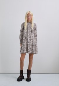 Vestido recto beige con estampado floral, de mangas largas y escote fruncido, combinado con botas negras de tobillo grueso. Textura suave por toda la prenda.