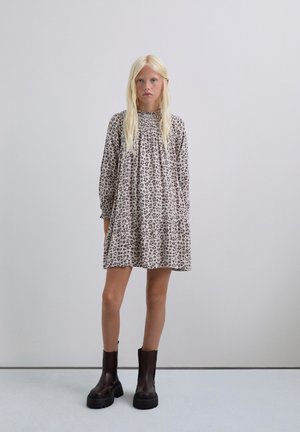 Vestido recto beige con estampado floral, de mangas largas y escote fruncido, combinado con botas negras de tobillo grueso. Textura suave por toda la prenda.