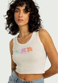 Weißes, kurz geschnittenes Tanktop mit gerippter Textur, das ein mehrfarbiges Blumendesign in sanften Blau-, Pink- und Orangetönen zeigt.