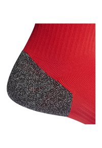 Calcetín rojo con un talón reforzado texturizado en negro y gris. La parte superior presenta un diseño liso y acanalado, exhibiendo una estructura sin costuras.