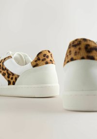 White sneakers with leopard print accents on the heel. Smooth leather material with soft textured finish on the leopard section. Rubber sole.
