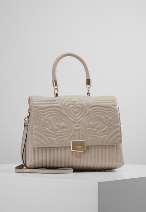 Beige læderhåndtaske med quiltede blomster- og hjerteprint, guldfarvet spænde, topgreb og aftagelig skulderrem på en hvid overflade.