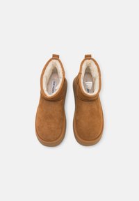 Bocanci din piele întoarsă maro, cu căptușeală pufoasă de culoare crem, vârf rotunjit și o mică buclă la spate pentru o montare ușoară. Design simplu, talpă din cauciuc plat.