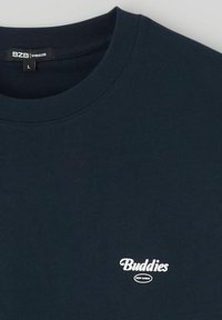 T-shirt oversize bleu marine en coton, avec un col rond et un logo "Buddies" blanc imprimé sur la poitrine.
