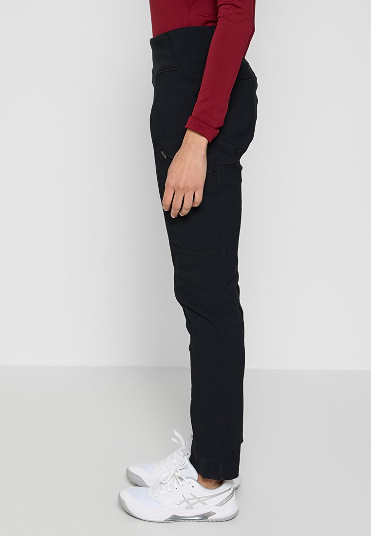 Czarne, dopasowane spodnie o eleganckim fasonie, z wysokim stanem, bocznymi kieszeniami i gładką teksturą. Noszone z białymi butami sportowymi.