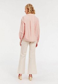 Chemisier rayé léger en rose et blanc, avec une coupe décontractée et des manches à manchette, associé à un pantalon évasé crème et des talons blocs beiges.