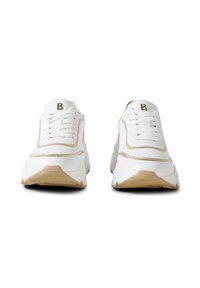 Bílé tenisky s béžovým lemováním a podrážkami, zepředu zobrazující tkaničky a kovové logo "B" na jazycích, na bílém pozadí.