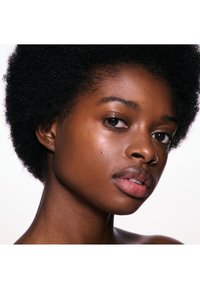 Nærbillede af en ung sort kvinde med naturlig afrofrisure, glat hud og en næsesmykke, der ser let til venstre mod en hvid baggrund.