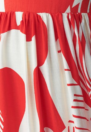 Červená a biela tkanina s vzorom, ktorá obsahuje abstraktné tvary, s textúrovaným, skladaným dizajnom v oblasti pásu. Mäkko splývavý, ľahký materiál.