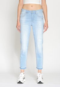 Ljusblå denimjeans med tapered passform, med slitna detaljer på benen och fransade fållar. Matchas med vita sportskor.