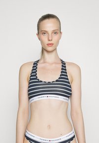 Soutien-gorge de sport à rayures noir et blanc avec un décolleté en scoop et un dos nageur. Présente une bande logo et de subtils accents circulaires le long des rayures.