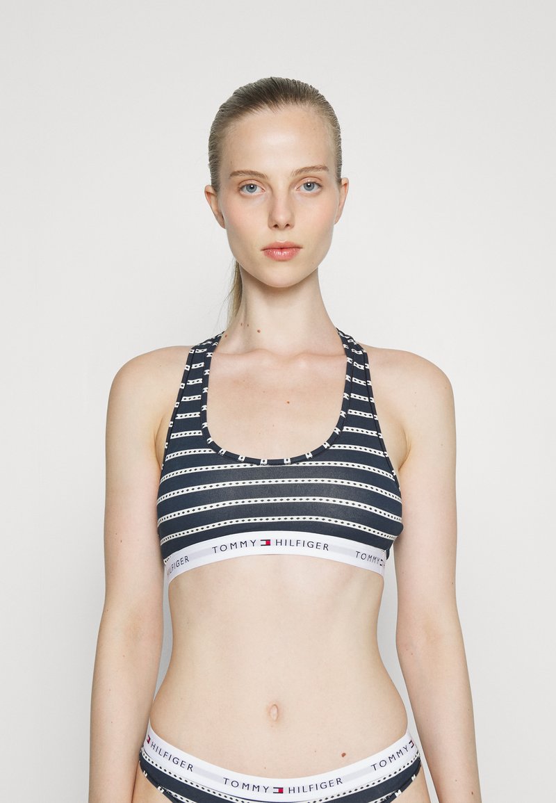 Soutien-gorge de sport à rayures noir et blanc avec un décolleté en scoop et un dos nageur. Présente une bande logo et de subtils accents circulaires le long des rayures.