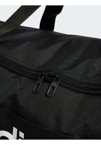 Schwarze Reisetasche mit einem Reißverschluss, ausgestattet mit zwei schwarzen Reißverschlusszügen und einer glatten, strukturierten Oberfläche. Logo in Weiß auf der Vorderseite angebracht.
