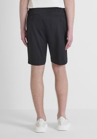 Pantaloni corti neri con una texture liscia, elastico in vita e dettagli sulla tasca posteriore, abbinati a scarpe da ginnastica bianche.