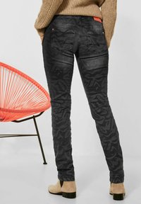 Svarta mönstrade jeans med slim fit, som har en lätt lyster och två bakfickor. Bärs tillsammans med en tan-färgad tröja och ankelstövlar.