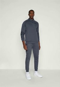 Grau, Langarm-Pullover mit Reißverschluss am Hals und passenden schmalen Hosen. Der Stoff hat eine glatte Textur und weist ein Logodetail an den Ärmeln auf.