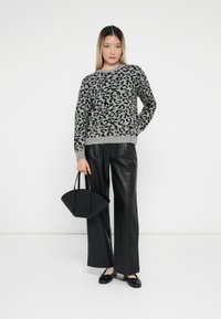 Pull en imprimé léopard gris avec des manches longues, associé à un pantalon taille haute en cuir synthétique noir. Le modèle tient un petit sac à main noir.