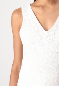 Weißes Spitzen-Top mit V-Ausschnitt, floralem Muster und strukturiertem Material, entworfen mit einer figurbetonten Silhouette und breiten Trägern.
