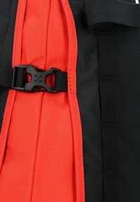 Tejido de nylon negro y rojo, con un panel central rojo, correas laterales y un resistente hebilla de plástico negra para un cierre seguro.