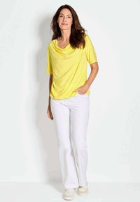 Geel gedrapeerd top met korte mouwen, gecombineerd met witte flared broeken en witte sneakers. Soepele stof met een losse pasvorm.