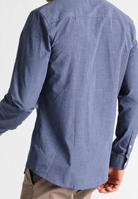 Tył koszuli z długim rękawem w kolorze granatowym, wykonanej z teksturowanego materiału, z mankietami na pojedynczy guzik i zaokrąglonym dołem.