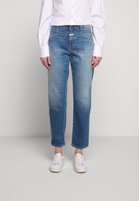 Ljusblå denimjeans med avslappnad passform, raka ben, minimal blekning och femfickdesign, kombinerat med vita sneakers.