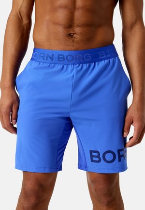 Hombre vistiendo pantalones cortos deportivos azul brillante con cinturilla elástica y marca "BJÖRN BORG" en la cinturilla y la pierna.