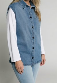 Denim button-up shirt with a light blue wash, black buttons, and a collared neck. Pairing with a white long-sleeve shirt underneath.