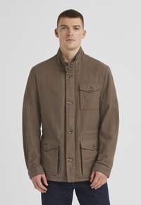 Leichte braune Jacke mit hohem Kragen, vorderem Knopfverschluss und zwei aufgesetzten Taschen. Verfügt über einen strukturierten Stoff und subtile Nähedetails.