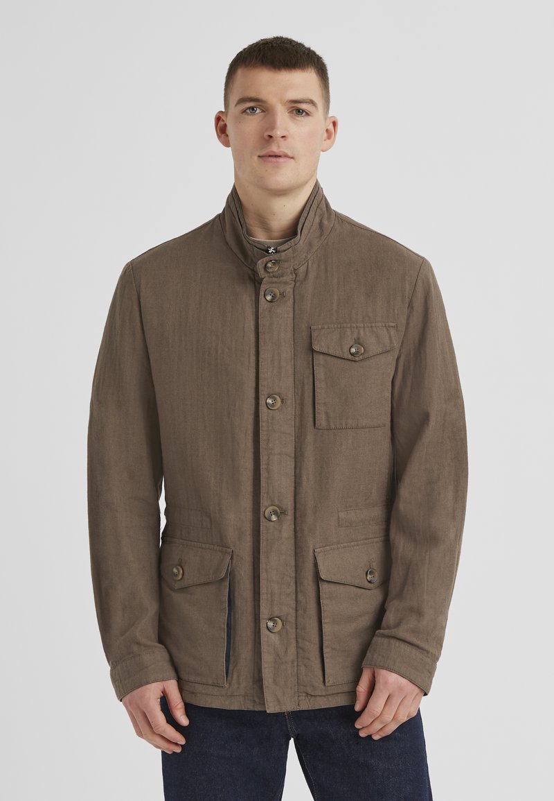Leichte braune Jacke mit hohem Kragen, vorderem Knopfverschluss und zwei aufgesetzten Taschen. Verfügt über einen strukturierten Stoff und subtile Nähedetails.