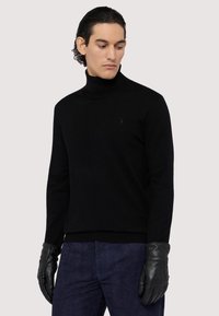 Svart turtleneck-sweater i mjukt material med en subtil logotypdetalj. Matchad med svarta läderhandskar och marinblå strukturerade byxor.