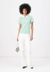 Πράσινο και άσπρο ριγέ polo μπλουζάκι με γιακά, συνδυασμένο με λευκά φαρδιά παντελόνια. Το μοντέλο κρατά μια μικρή πράσινη και ασημί τσάντα.