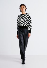 Maglione a righe bianco e nero con finitura texture, scollatura rotonda e maniche lunghe, abbinato a pantaloni in pelle nera e stivaletti.