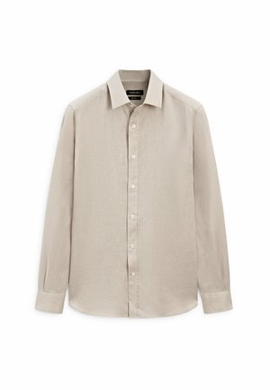 Chemise beige à manches longues avec col boutonné, fabriquée en tissu texturé, dotée d'une patte de boutonnage à l'avant avec des boutons blancs et un ourlet arrondi.