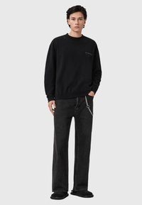 Μαύρο φούτερ με ριμπ μανσέτες, συνδυασμένο με σκούρο τζιν τζιν που διαθέτει λεπτομέρεια αλυσίδας. Το μοντέλο φοράει μαύρα παντόφλες. Απλός και λιτός σχεδιασμός.