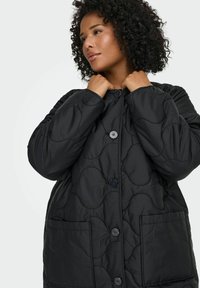 Juoda siūta striukė su apvaliais siūlais, užsegama sagomis, dvi priekinės kišenės. Minkšta tekstūra, laisvas oversized siluetas ir aukštas apykaklės dizainas.