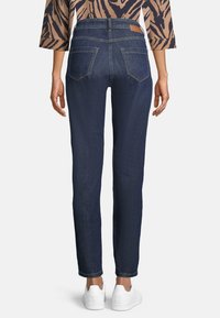 Mörkblå raka jeans med en mjuk textur, bakfickor och en läderlapp i midjan; kombinerat med vita sneakers.