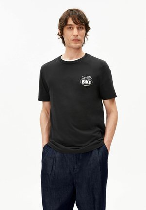 Schwarzes Baumwoll-T-Shirt mit einem grafischen "GET ON BIKE"-Logo auf der linken Brust und einem runden Halsausschnitt, kombiniert mit dunkelblauen, plissierten Hosen.