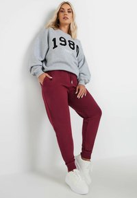 Grijze sweatshirt met de tekst "1980 PARIS" en bordeaux joggingsbroek. Witte sneakers. Zachte stof. Casual ontwerp met elastische boorden en tailleband.