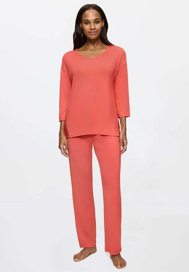 Ensemble de sommeil corail comprenant un haut ample à col en V avec des manches trois-quarts et un pantalon droit assorti, fabriqué en tissu doux et lisse.