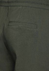 Shorts vert olive avec une texture lisse, dotés d'une taille élastique et d'une seule poche arrière sans matériel visible.