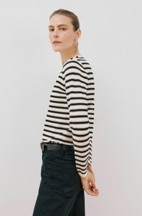 Schwarz-weiß gestreiftes Langarmoberteil aus leichtem Stoff, enganliegendes Design, kombiniert mit schwarzen Hosen, die über einen schmalen Gürtel verfügen.