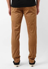 Pantalon en coton marron avec une coupe droite ; dispose de poches en biais et d'une texture lisse ; associé à des chaussures basses noires.