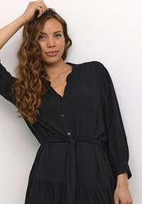 Schwarzes Hemdkleid mit V-Ausschnitt, langen Ärmeln und Taillenband. Verfügt über einen strukturierten Stoff und ein gestuftes Rockdesign.