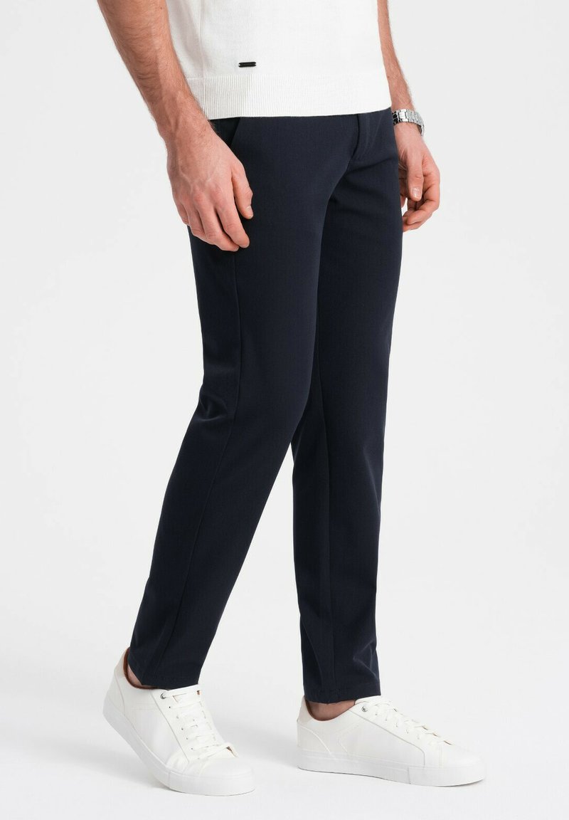 Navy broek met een getailleerde pasvorm, voorzien van een gladde textuur en een subtiele plooi, gecombineerd met witte sneakers.