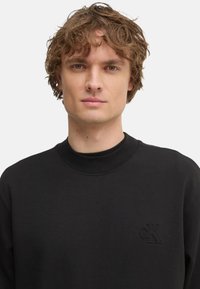 Sudadera negra hecha de un tejido suave, con cuello redondo, mangas largas y logotipo "cK" en relieve en el pecho. Textura suave.